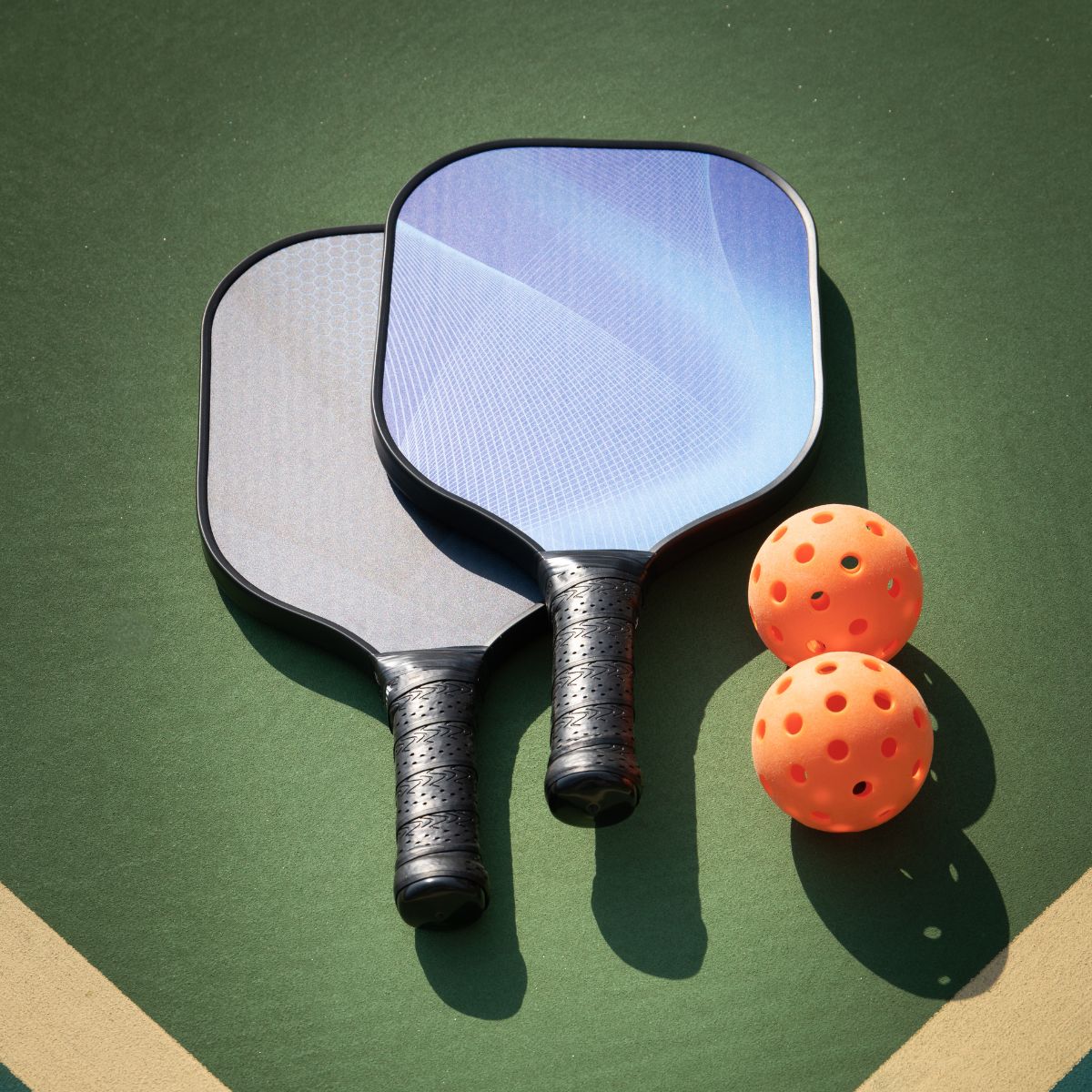 two pickleball paddles and two pickleballs sitting on court